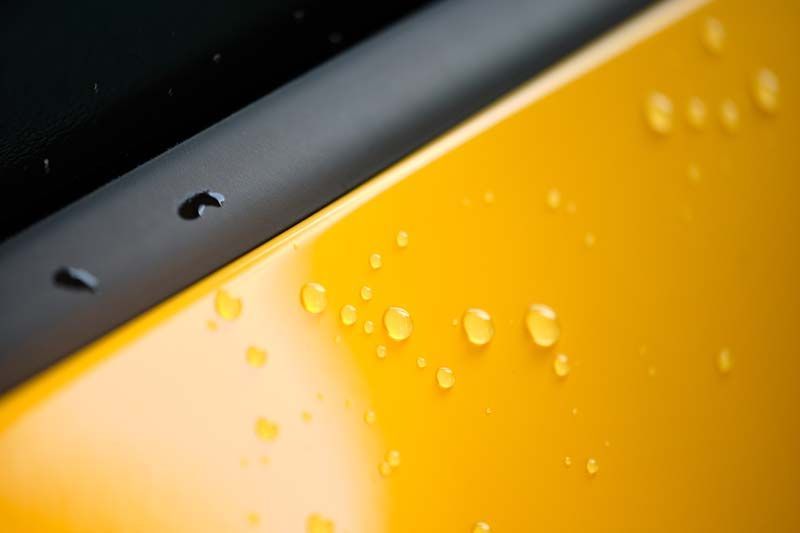 Close-up of yellow car surface with water droplets next to a black trim.