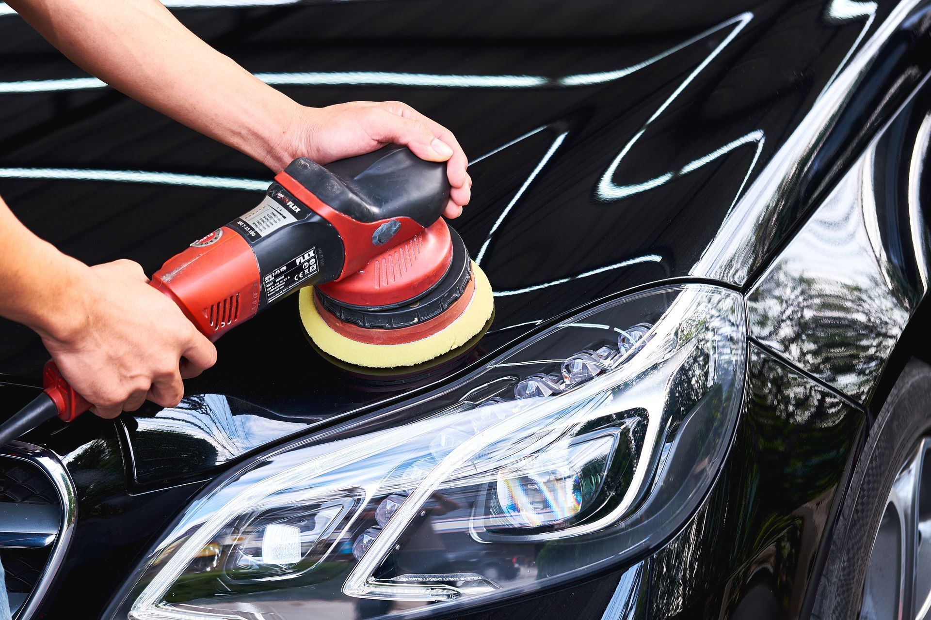 Person polishes black car hood with an electric buffer and pad.