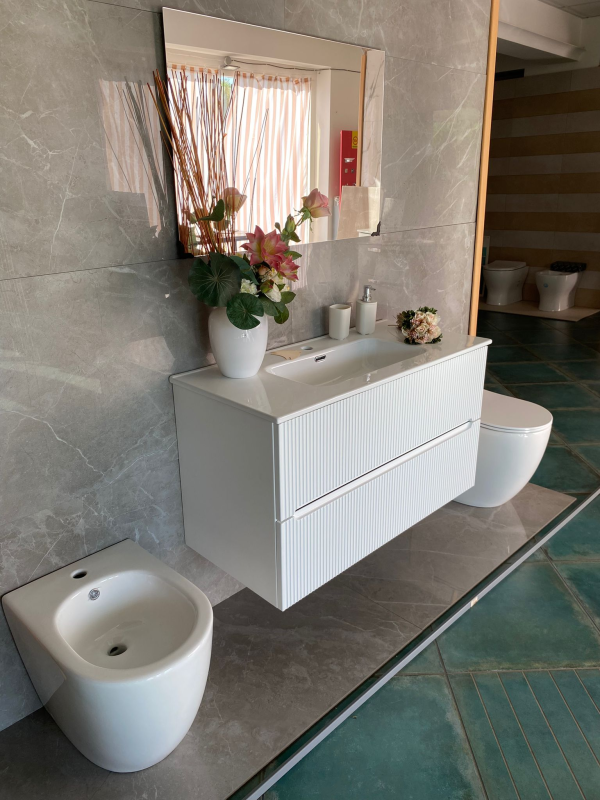 Moderno bagno bianco con mobile lavabo sospeso, WC e bidet. Pavimento e pareti piastrellati grigi.