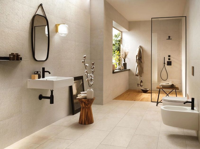 Bagno moderno dai toni neutri con lavabo sospeso, doccia, bidet e dettagli in legno. La luce naturale filtra all'interno.
