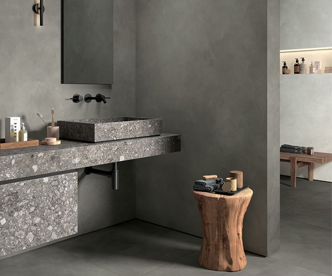 Bagno grigio con lavandino in pietra, sgabello in legno e arredamento neutro.