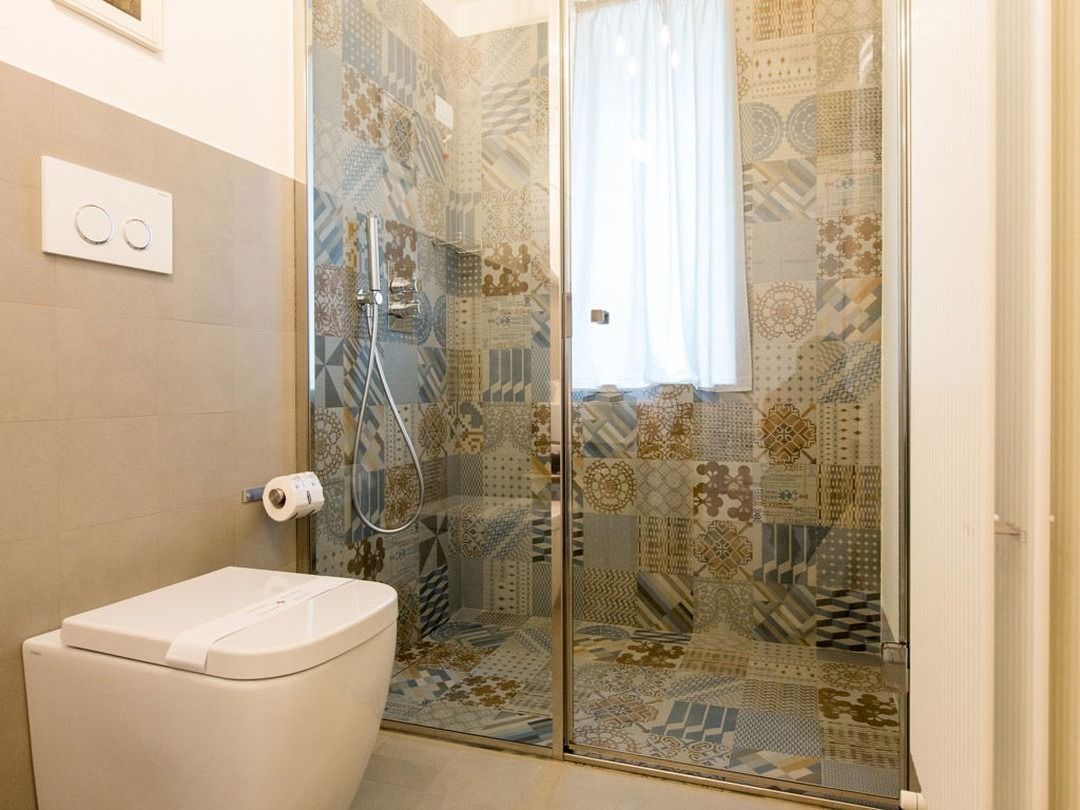 Bagno con doccia piastrellata, WC e pareti dai colori chiari.