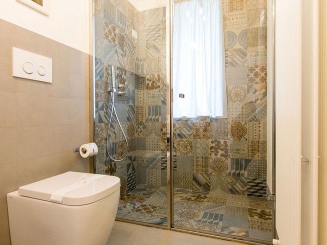 Bagno con doccia a fantasia, WC e pareti grigio chiaro.
