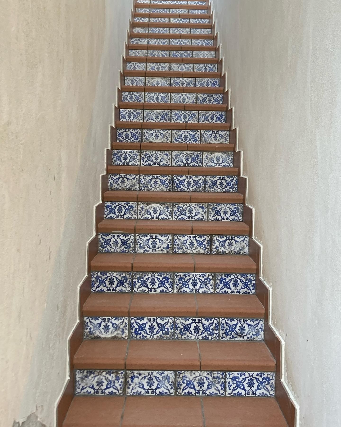 Scala con gradini marroni e piastrelle a motivi blu. Le pareti beige incorniciano la scala, che sale verso l'alto.