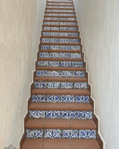 Scala con gradini marroni e piastrelle a motivi blu. Le pareti beige incorniciano la scala, che sale verso l'alto.