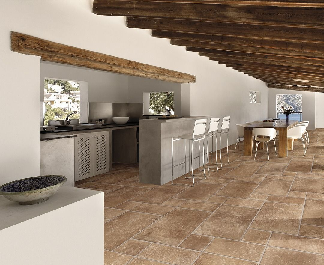 Ampia cucina con pavimenti in cotto, pareti bianche e travi in legno al soffitto.
