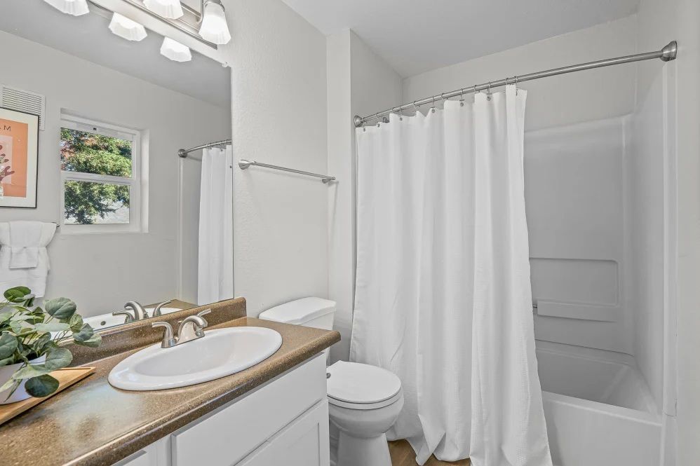 Bathroom with white walls, a bathtub, toilet, and sink, and a white shower curtain.