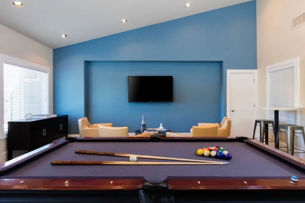 Pool table in a room with a blue accent wall, chairs, and a TV.