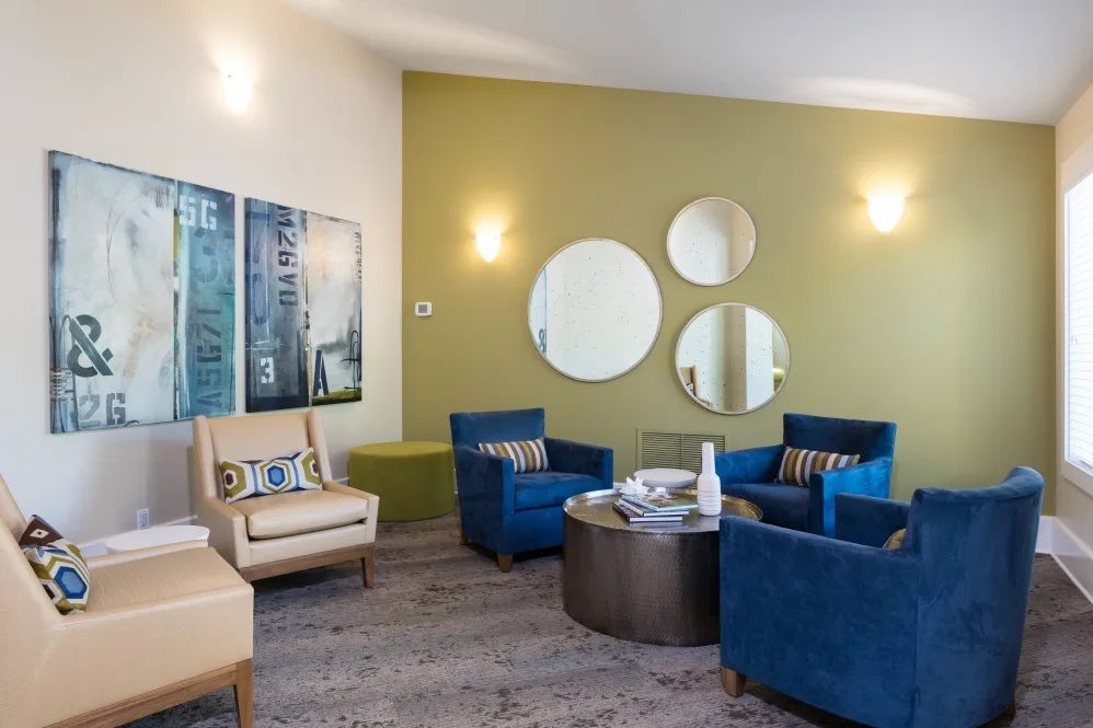 Lounge area with blue and tan armchairs, round mirrors on a green wall, and a low coffee table.