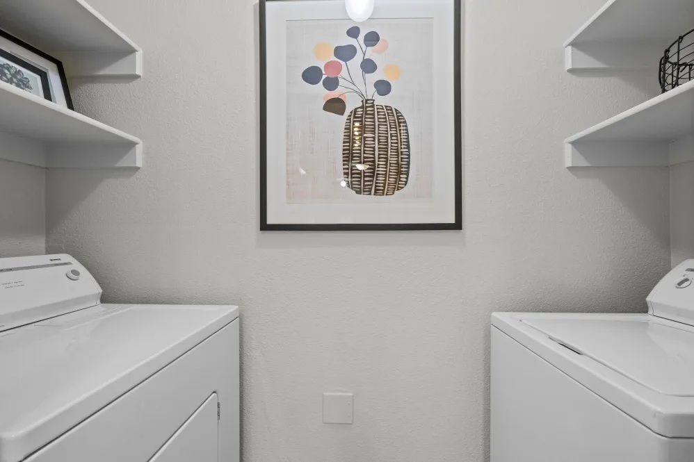 Laundry room with white washer and dryer, shelves, and art on the wall.