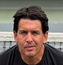 A man in a black shirt is sitting in front of a tennis net.