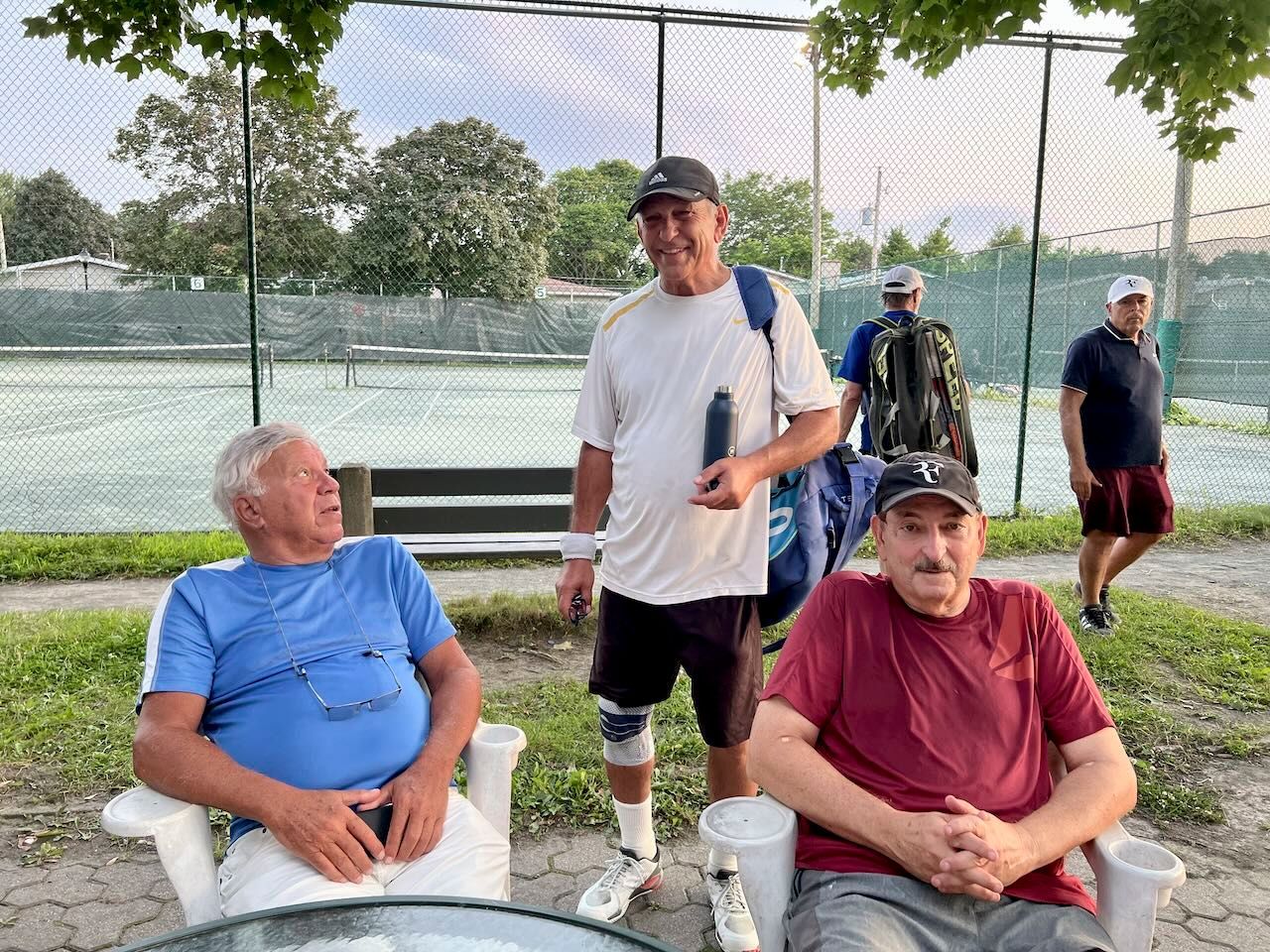 A group of men are sitting in chairs in front of a tennis court