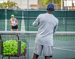 A man is standing on a tennis court watching a woman play tennis.