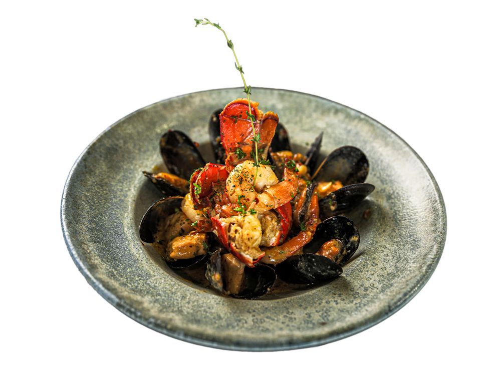 A seafood dish with lobster and mussels arranged in a bowl, garnished with a sprig of herb, on a grey plate.
