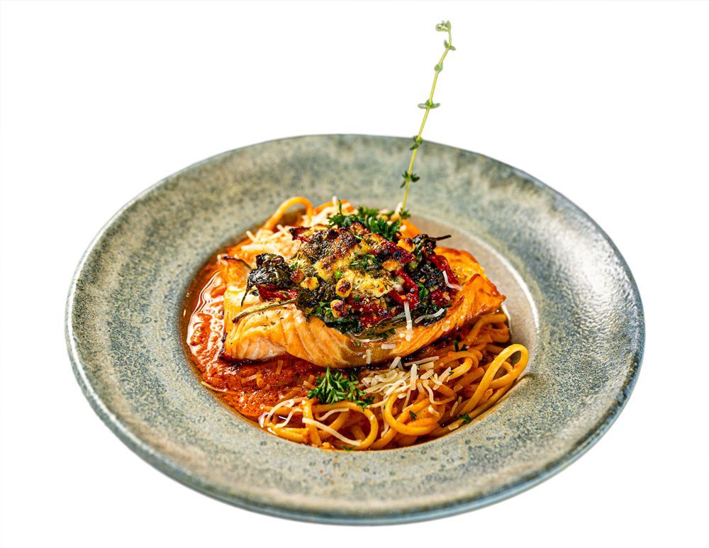 A seared salmon fillet served over tomato pasta in a textured grey bowl, garnished with herbs and grated cheese.