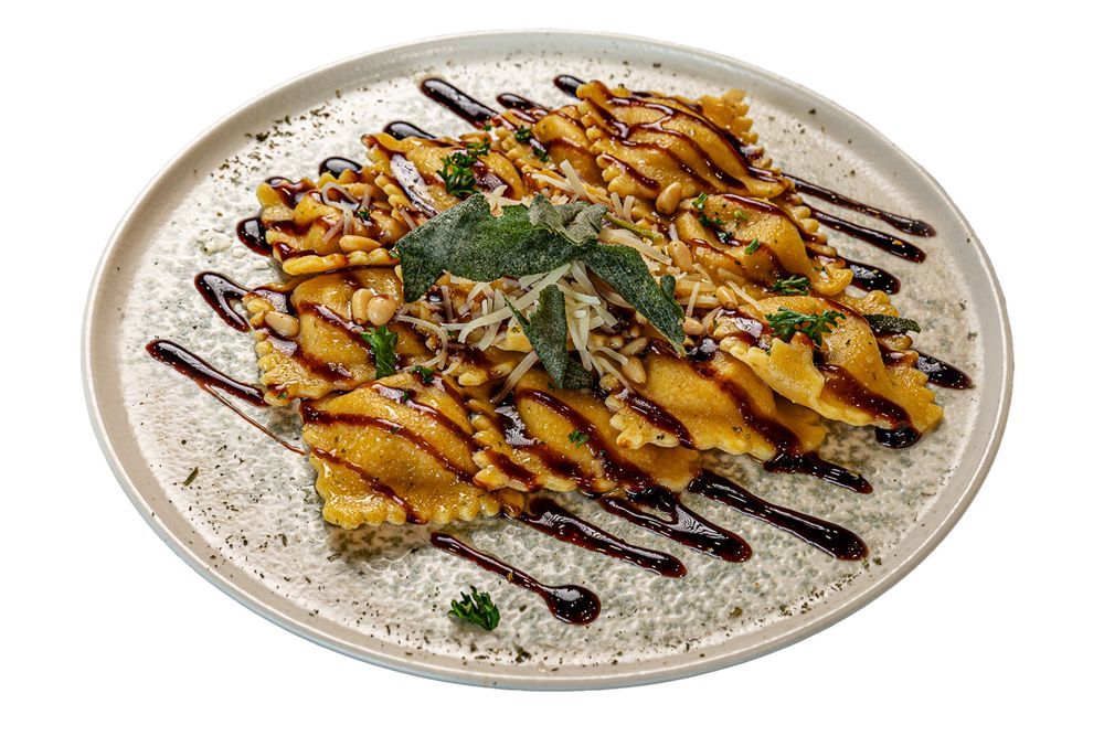 Ravioli served on a creamy sauce, drizzled with balsamic glaze, and topped with fresh herbs on a round white plate.