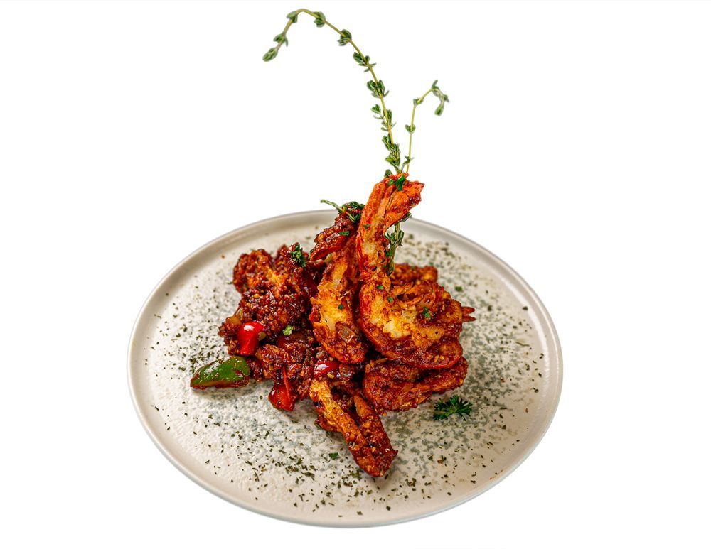 A plate of spicy, glazed jumbo shrimp garnished with fresh herbs, centered against a plain white background.