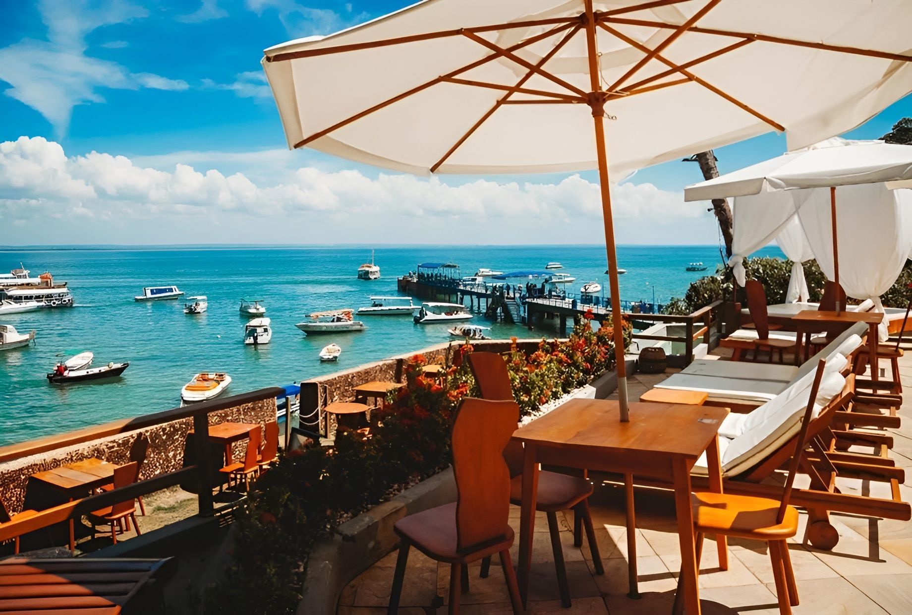 Um pátio com mesas, cadeiras e guarda-sóis com vista para o oceano. Hotel Portaló