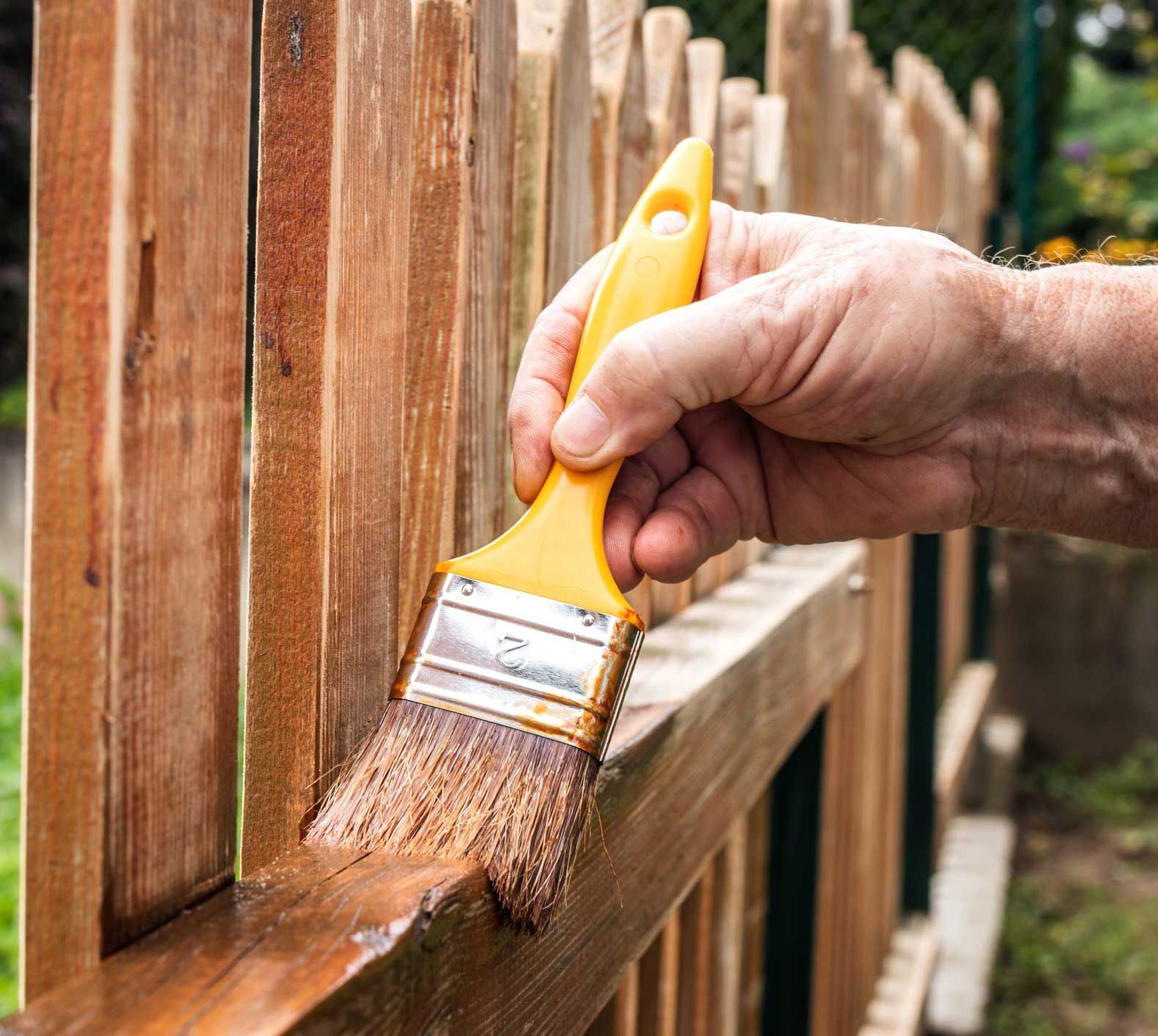 A person is painting a wooden fence with a brush.