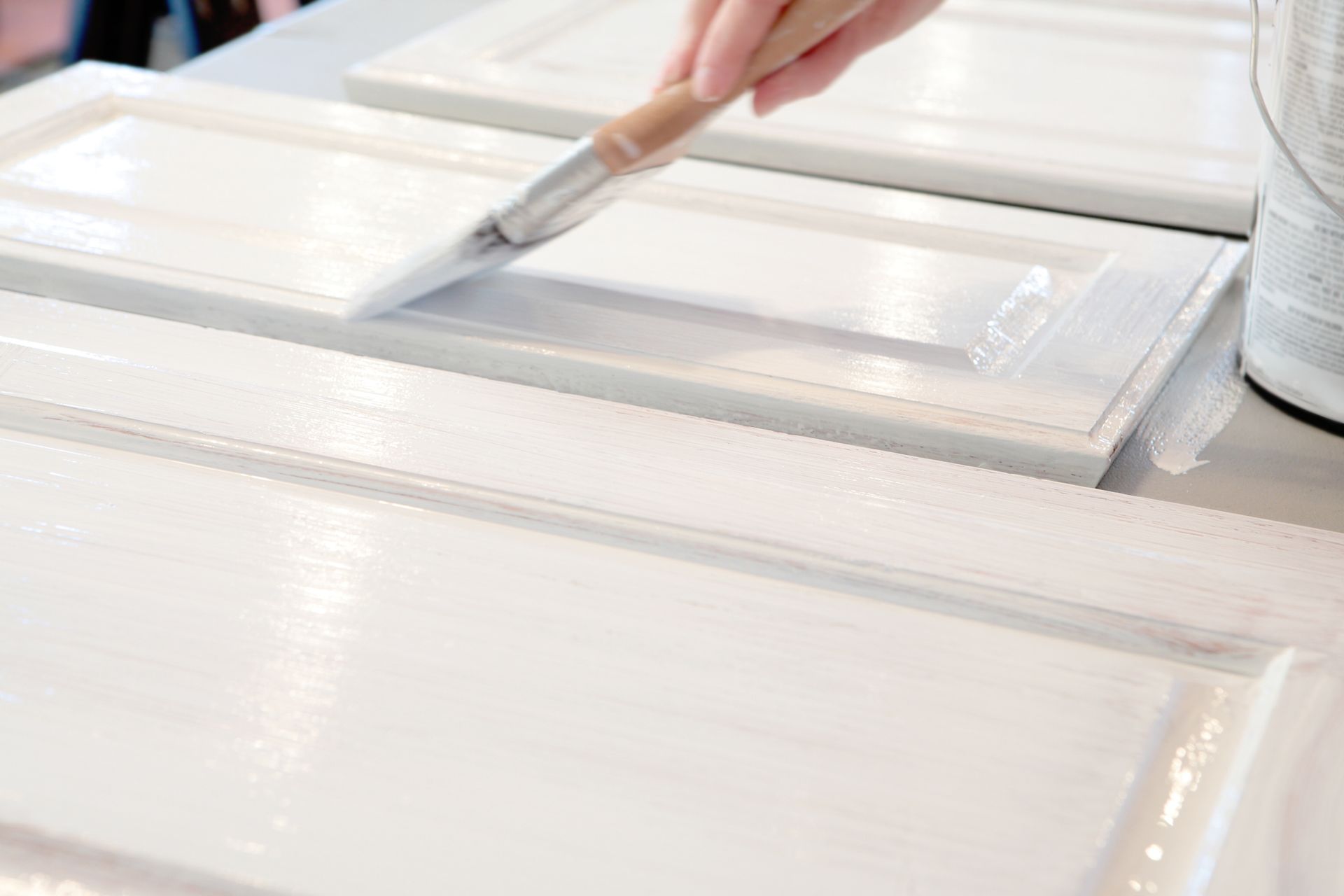 A person is painting a white cabinet door with a brush.