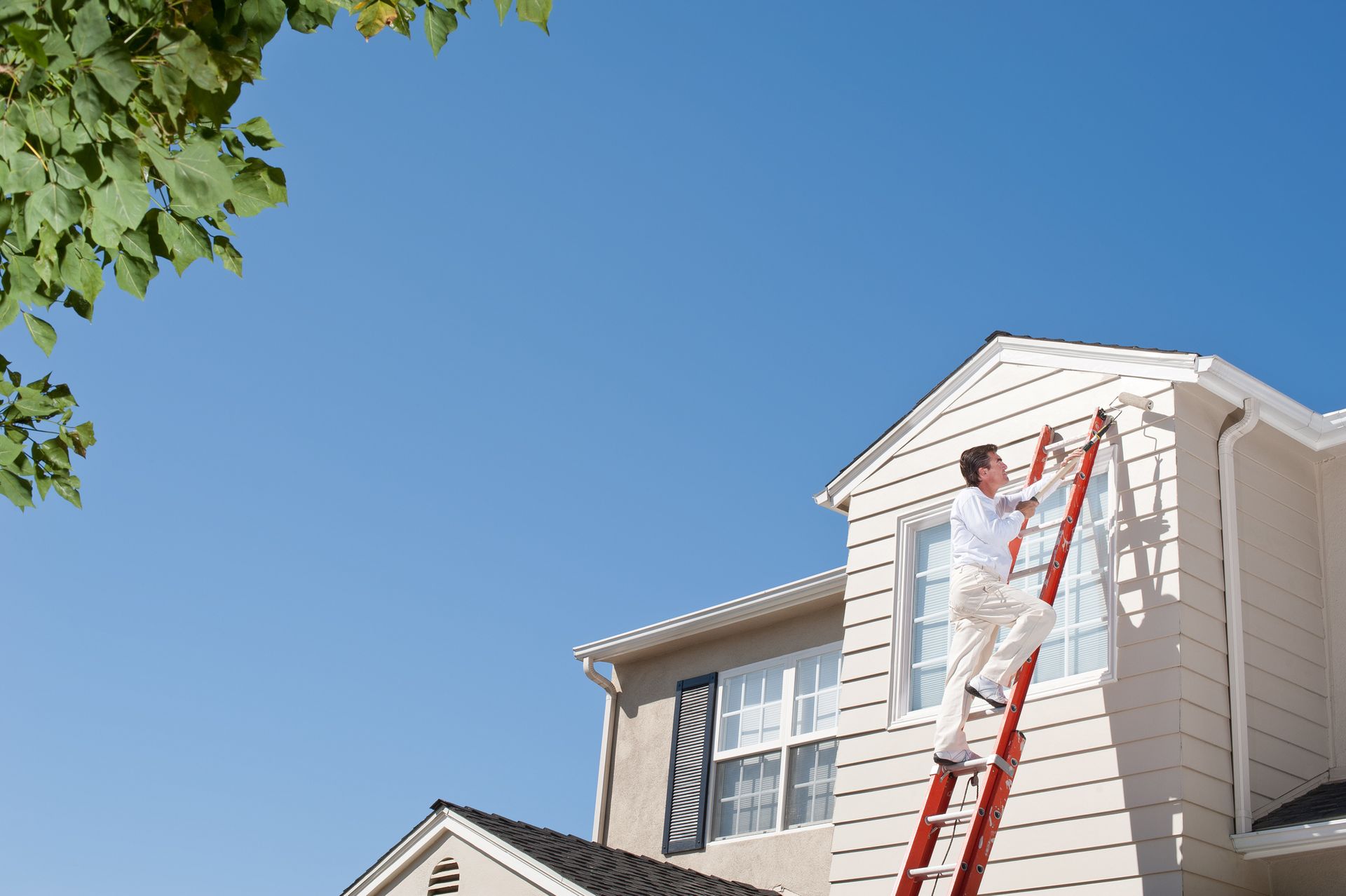 A man is standing on a ladder painting a house.