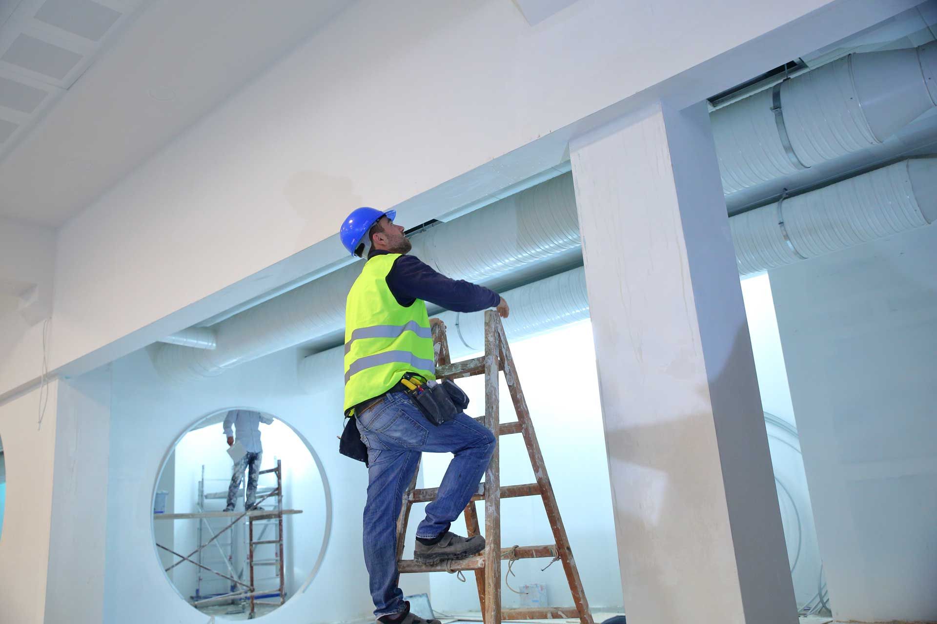 A man is standing on a wooden ladder in a room.