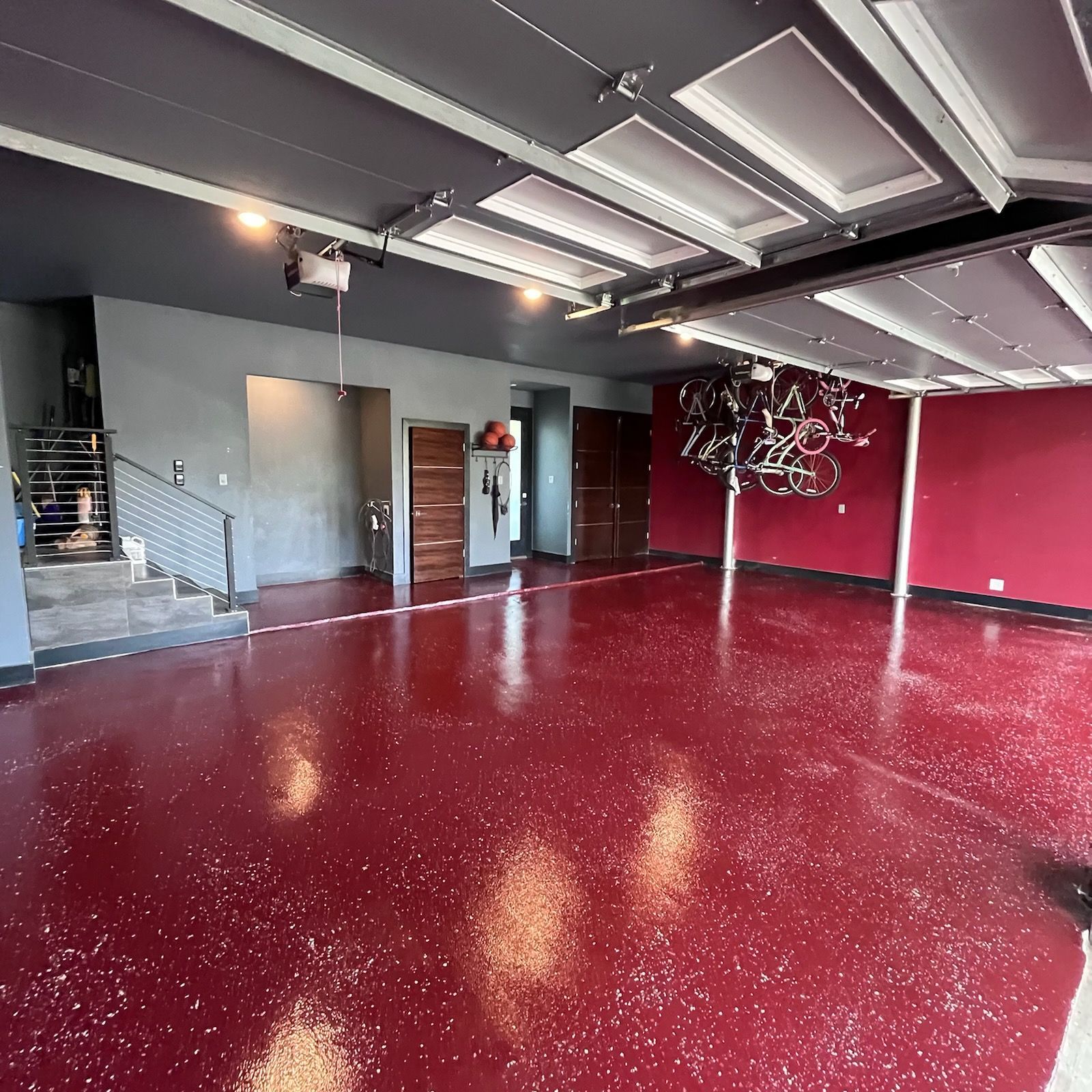 A large empty garage with a red floor and a bunch of bikes hanging from the ceiling.