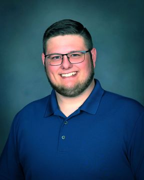 Smiling person in glasses wearing a teal shirt against a gray background