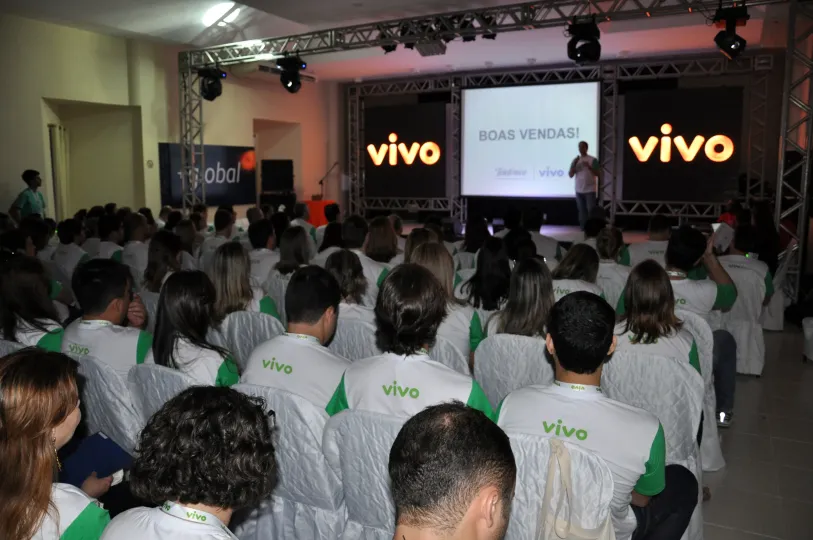 Um grande grupo de pessoas está sentado em frente a uma tela que diz vivo