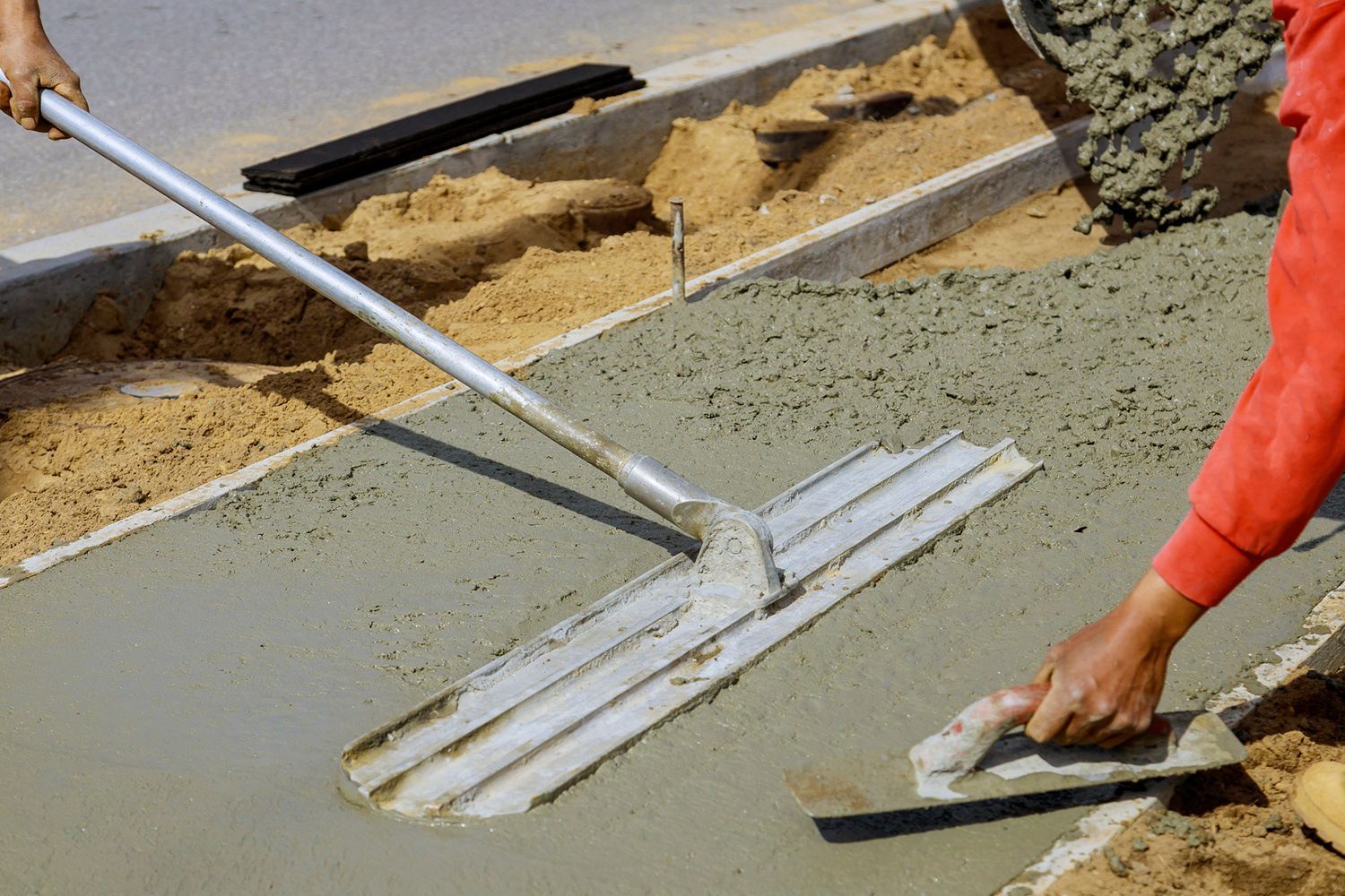 Workers smoothing wet concrete with a screed and trowel at a construction site. Workers smoothing wet concrete with a screed and trowel at a construction site.