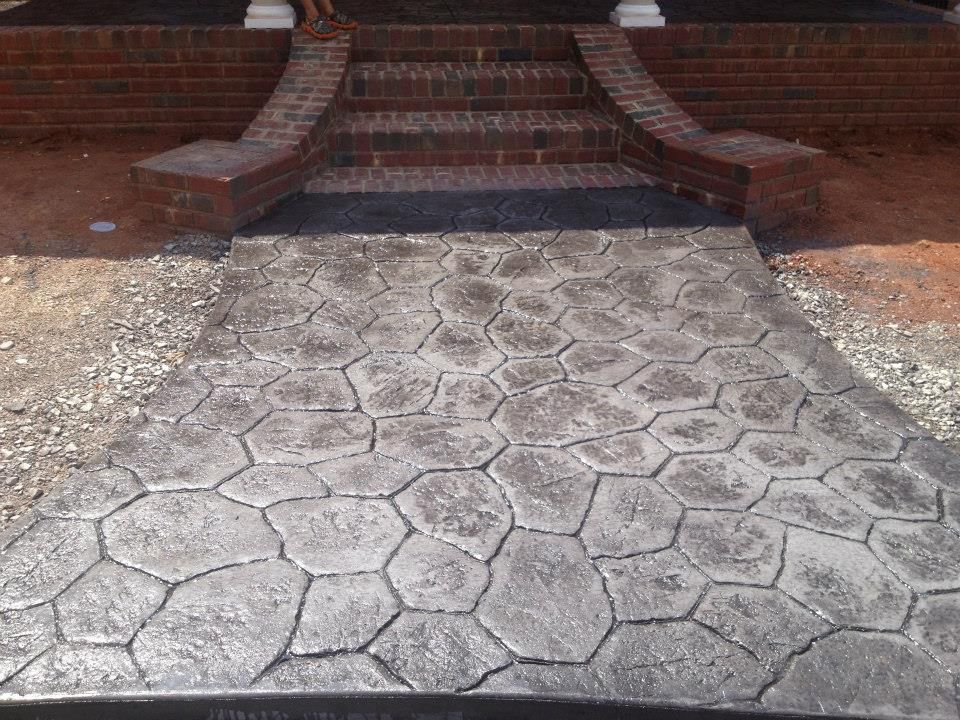 Stone-patterned concrete walkway leading to brick stairs and porch. Gravel and dirt surround the walkway.