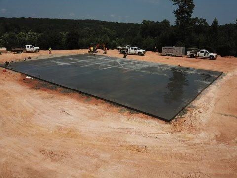 Newly poured concrete slab on a construction site; workers, trucks, and equipment present.