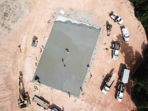 Aerial view of a rectangular concrete slab being poured at a construction site surrounded by vehicles and equipment.