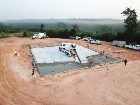 Concrete being poured at a construction site; workers guide the flow. Gray concrete, brown dirt, and white trucks.