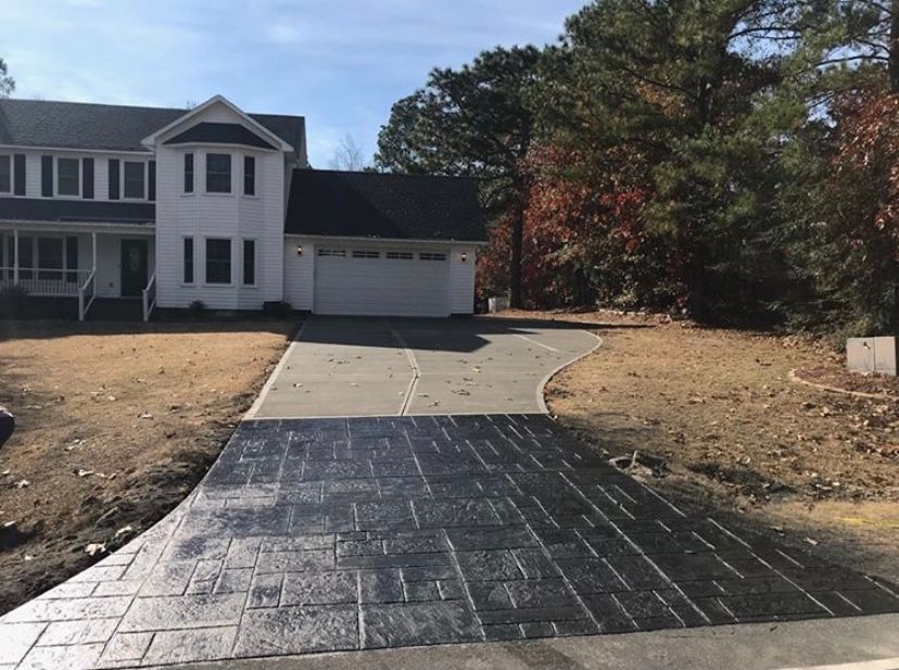 Two-story white house with new black stamped concrete driveway; trees in the background.
