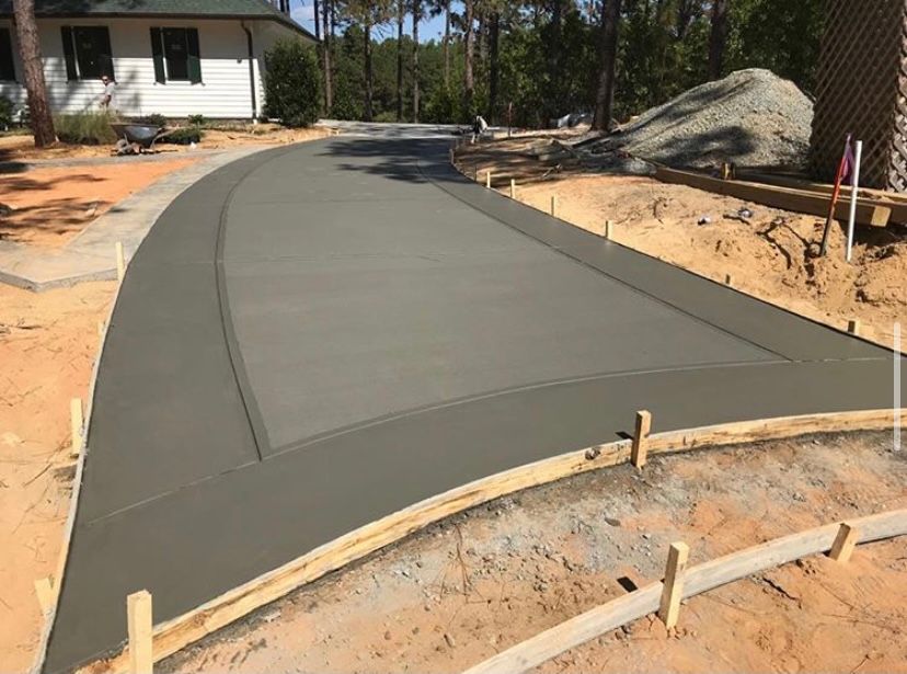 Freshly poured concrete driveway with wooden formwork, next to a house under construction.