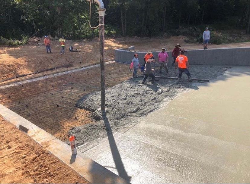 Concrete being poured by a pump truck onto a construction site. Workers wearing safety vests and helmets are present.