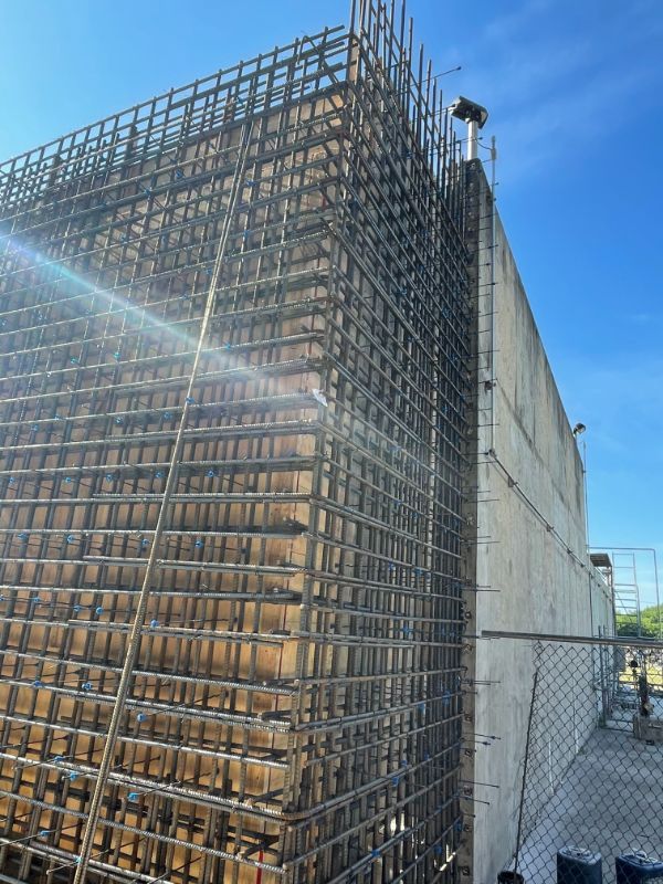 Reinforced steel rebar cage on a concrete wall under construction against a blue sky.
