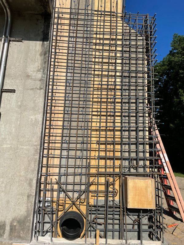 Steel rebar framework on a concrete wall, ready for pouring. Forms a grid shape around a drainage pipe.