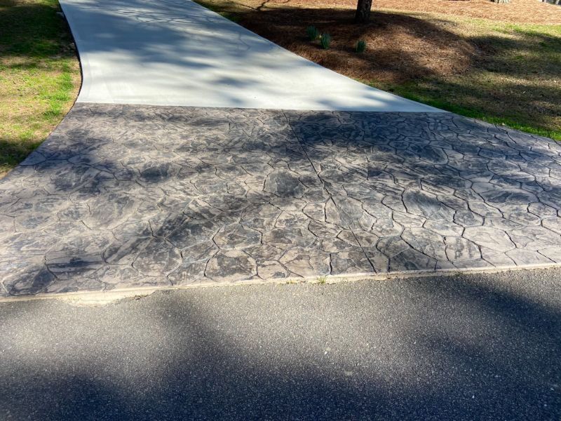 Paved walkway transitions from asphalt to textured concrete, then to a smooth concrete path, with grassy areas bordering.