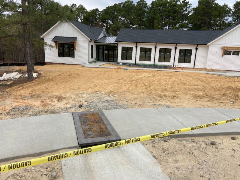 A newly constructed white house with black trim, surrounded by a dirt yard. Caution tape is across a concrete walkway.
