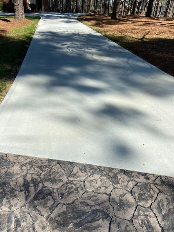 Gray concrete driveway with a stamped stone border, trees and grass.
