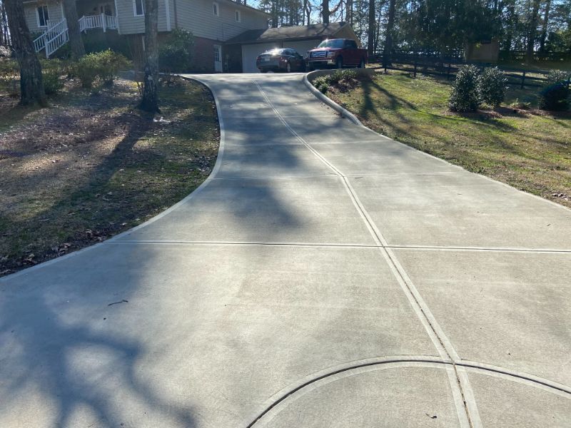 Concrete driveway leading to a house, with parked cars and surrounding green grass.