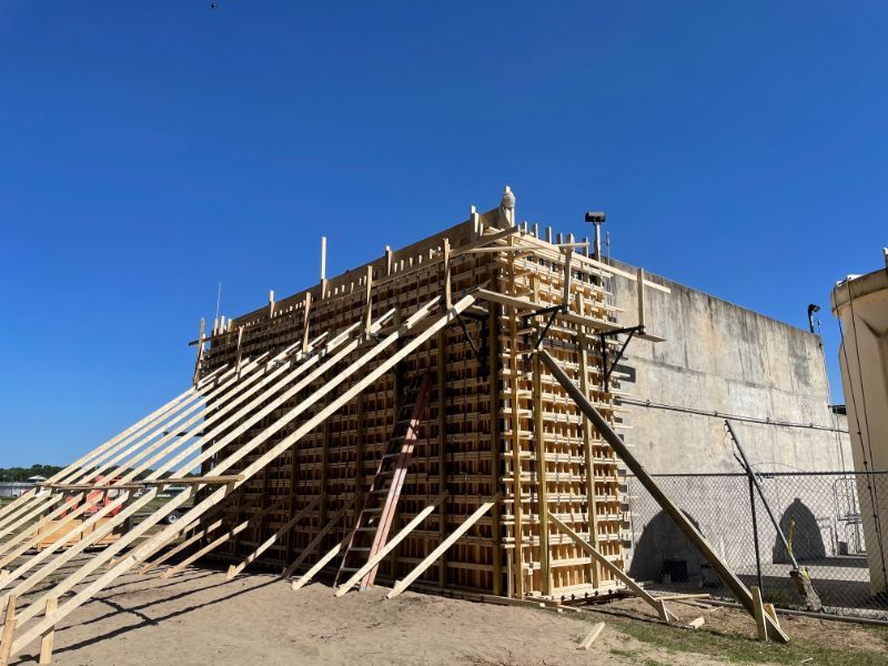 Wooden forms support a concrete structure under construction against a clear blue sky.