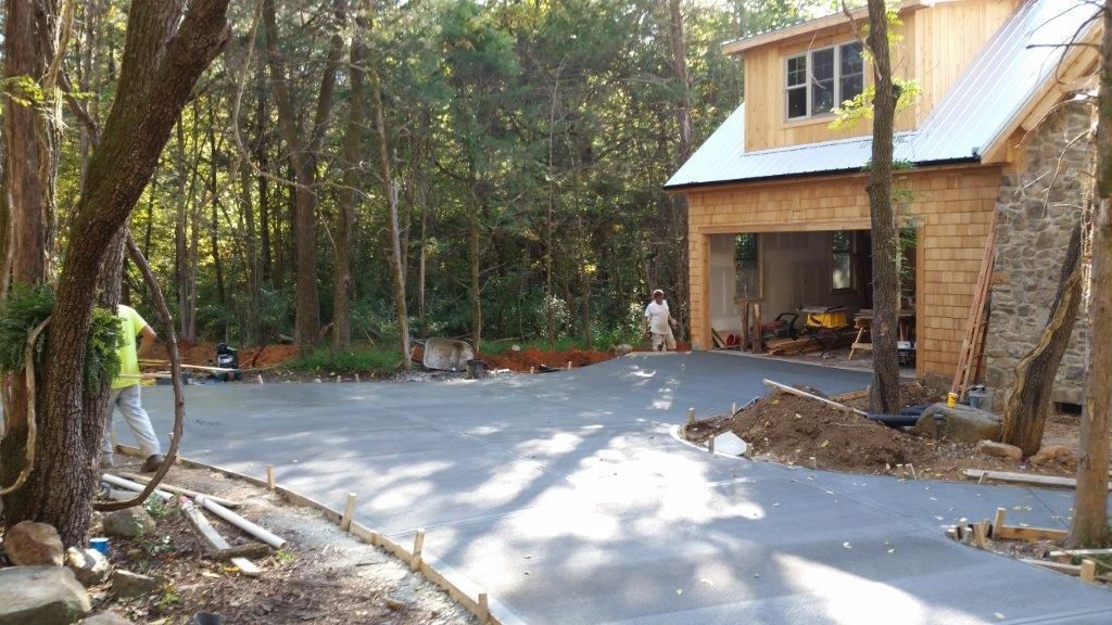 Driveway under construction with house, garage, and trees in background. Person working on the left.