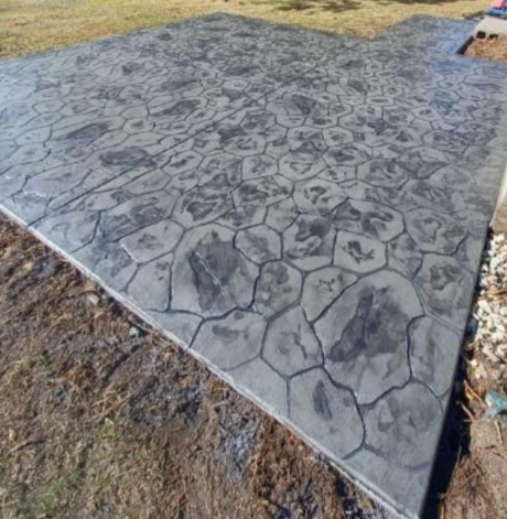 Black stamped concrete driveway leads to a white house with a two-car garage. Brown grass and trees surround. Black stamped concrete driveway leads to a white house with a two-car garage. Brown grass and trees surround.