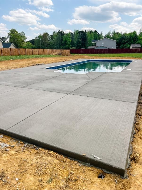 Concrete pool deck surrounding a rectangular pool filled with water, in a backyard setting. Concrete pool deck surrounding a rectangular pool filled with water, in a backyard setting.