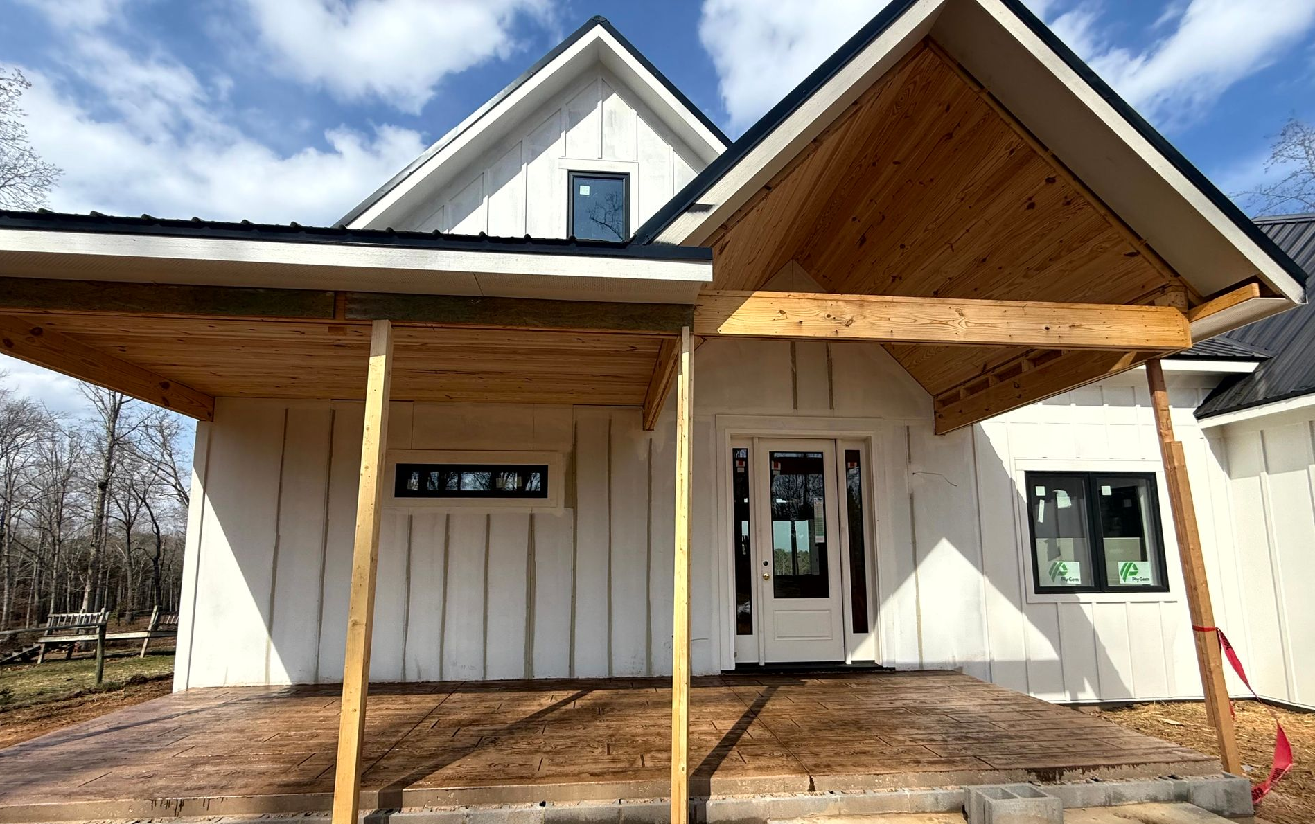 House under construction with a concrete ramp for accessibility. Tyvek wrap visible, worker on roof.