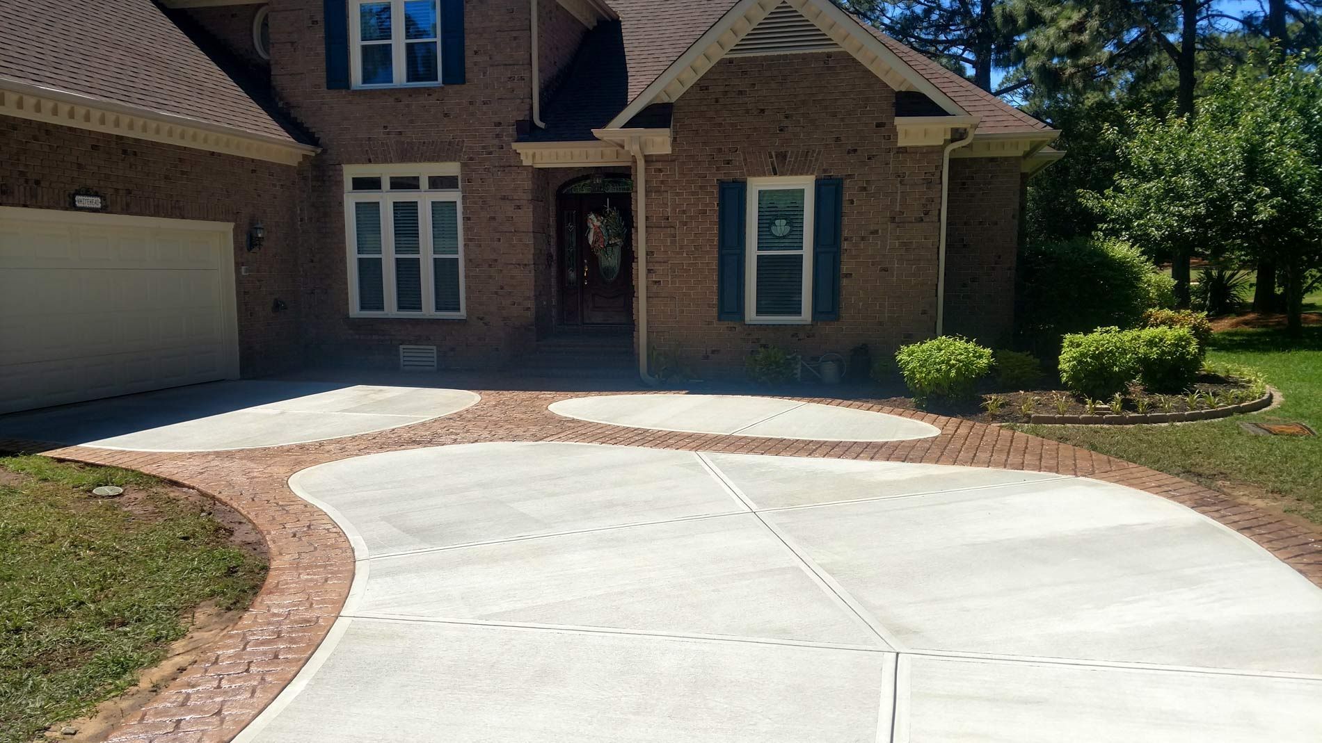 Brick house with concrete driveway, red brick border, and green lawn.