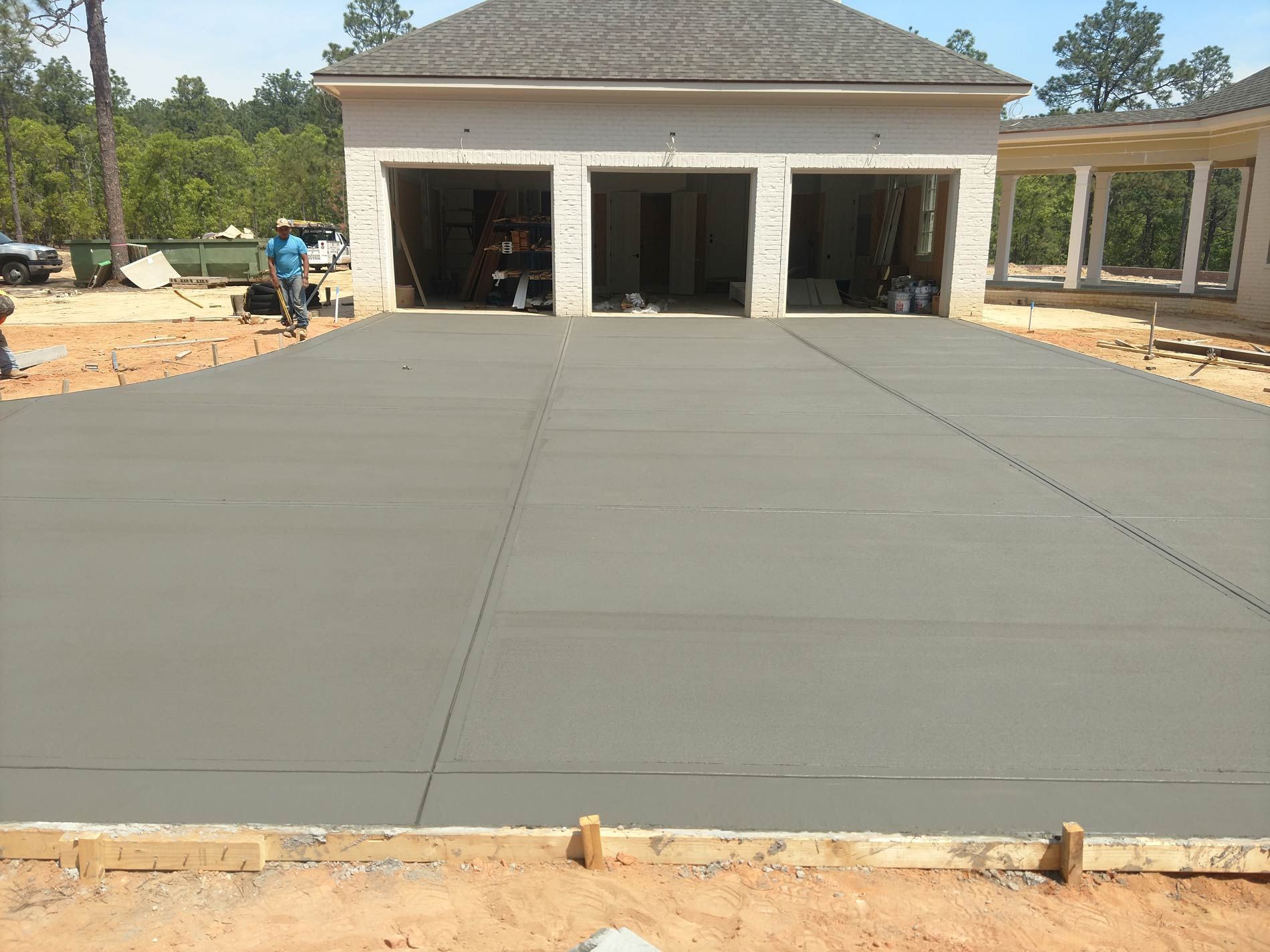 Newly poured concrete driveway in front of a three-car garage under construction.
